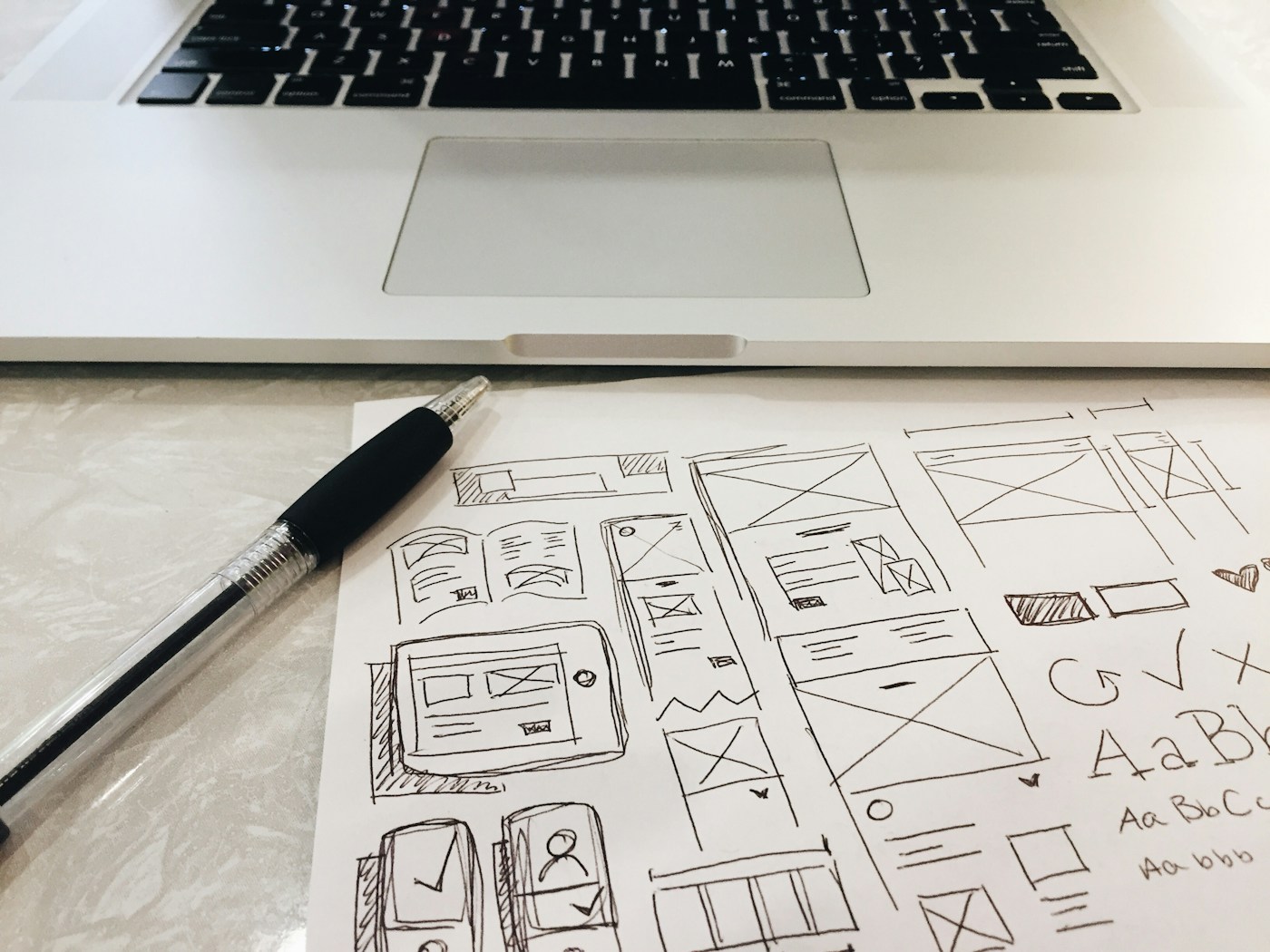 Pen sketches of website layouts on paper beside a laptop